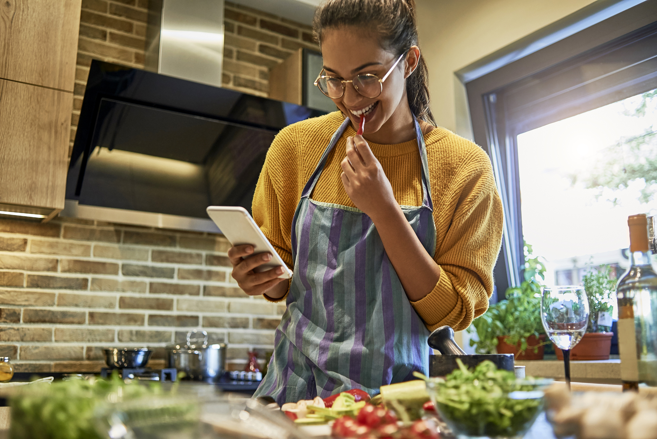 Young woman cooking and using her phone